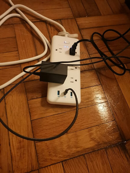 A power strip on the floor with cables plugged into it
