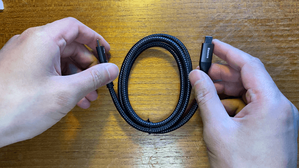 Somebody holding a coiled thunderbolt cable above a wooden table