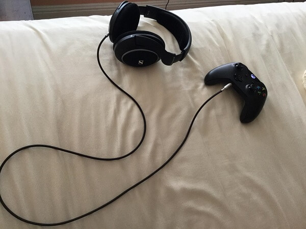 An audio cable plugged into a pair of Sennheiser headphones and an Xbox controller