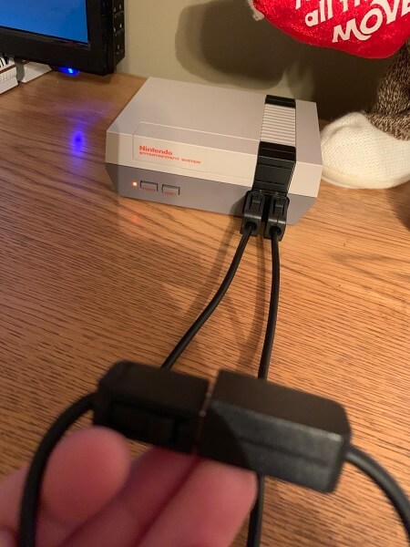 Somebody holding the connection between the extension and original cable, with the other end plugged into an NES in the background
