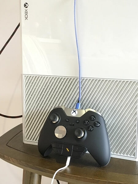 An Xbox controller with an adapter plugged in the bottom and a USB cable in the top, set standing on a Xbox