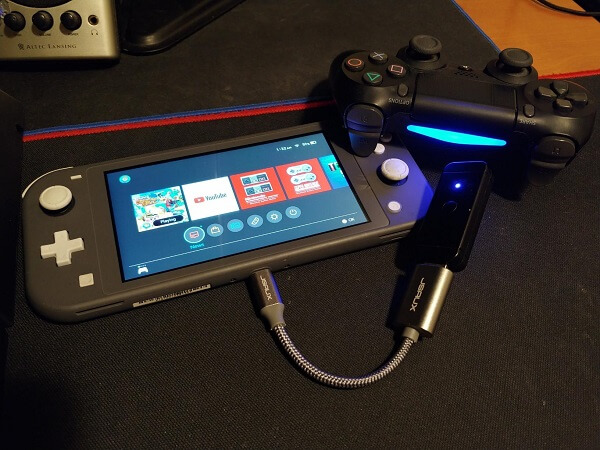 The adapter plugged into a USB extension cable, that is plugged into a Nintendo Switch, with a controller next to it