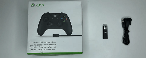 The adapter is set on a table, between an Xbox controller box and a USB cable