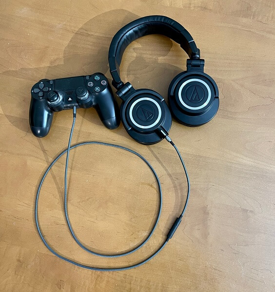 An audio cable plugged into a PS4 controller and a pair of headphones