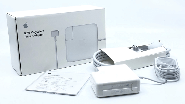 An Apple MagSafe power adapter on a desk next to the packaging