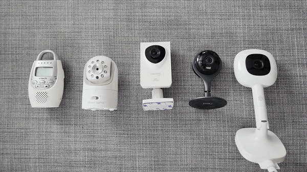 Different types of baby cameras laid out on a bed
