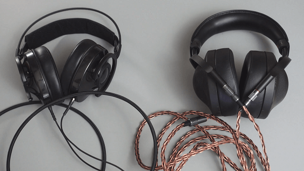 Two pairs of headphones on a desk with their cables around them